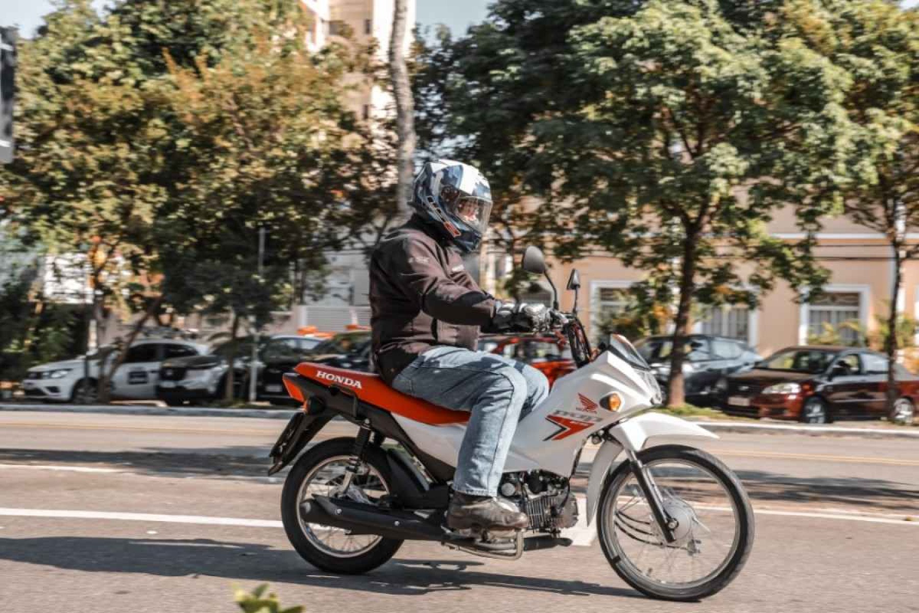 Honda Pop 110i 2025 branca com detalhes em vermelho e preto de lateral em movimento no asfalto