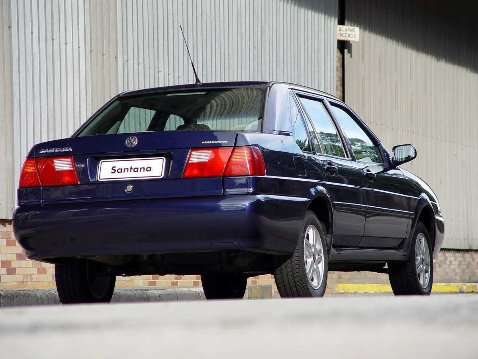 Volkswagen Santana azul, de traseira, estacionado em frente a galpão