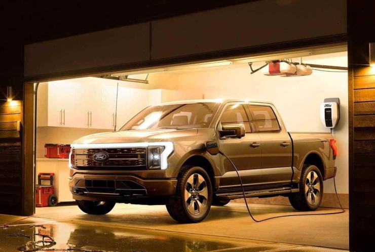 Caminhonete Ford F150 Lightning cinza, de frente, dentro de garagem iluminada, ligada a carregador de carros el&eacute;tricos