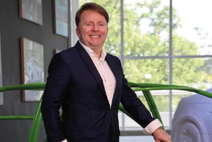 Homem branco com cabelo loiro curto penteado para o lado esquerdo. A pessoa est&aacute; vestida com blazer reto e camisa social branca segurando a estrutura de carro.  