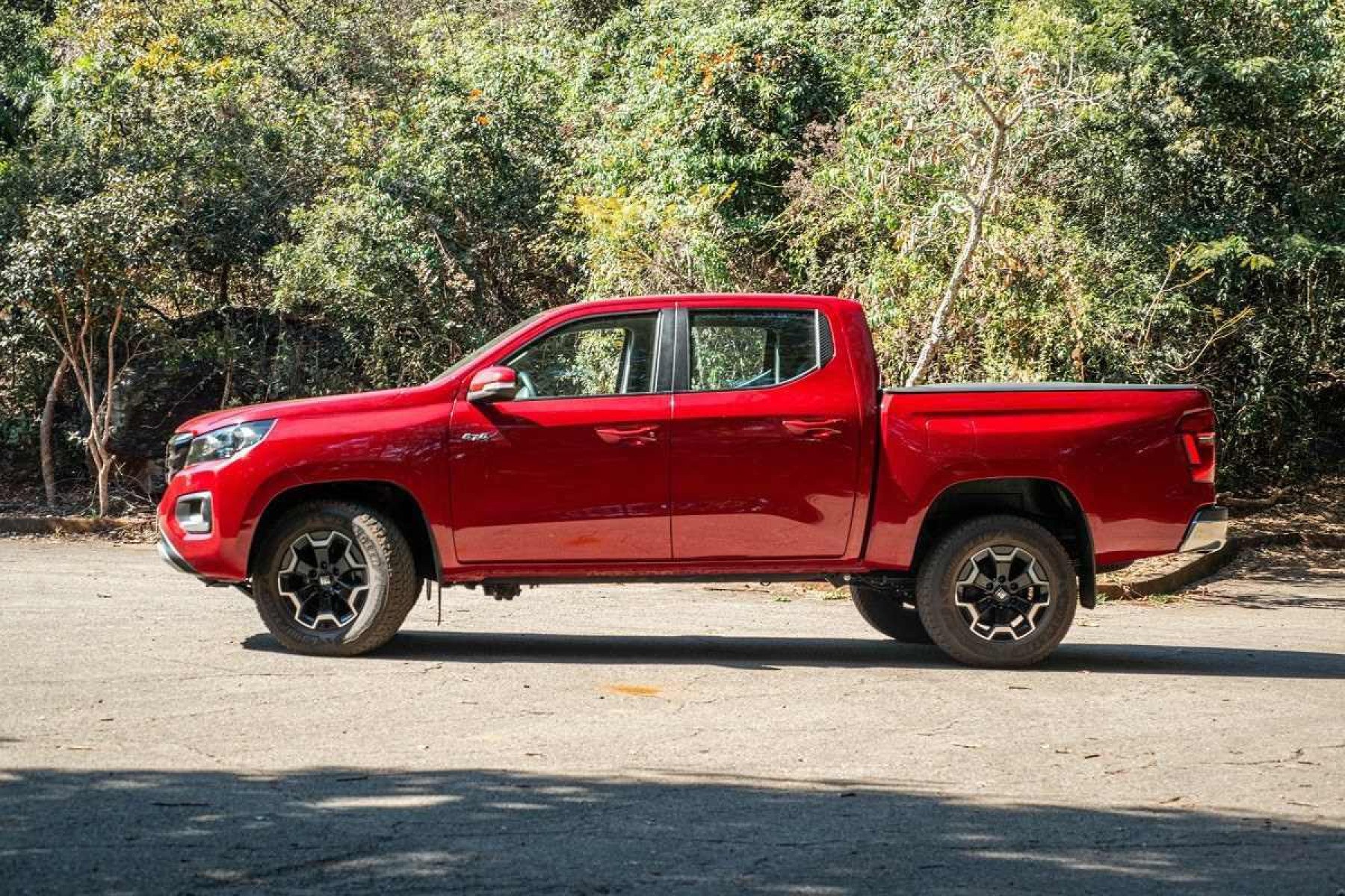 Vulcão Fiat Titano vermelho, de lado, estacionado em local asfaltado, com vegetação ao fundo