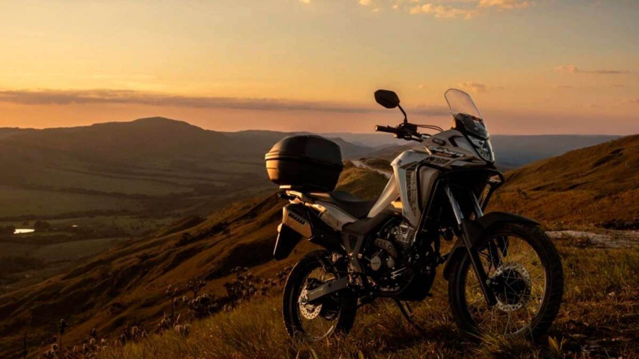 Moto Honda Sahara 300, parada de frente em 45 graus, em uma montanha com por do sol ao fundo