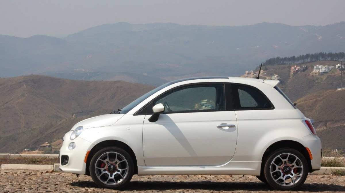 Fiat 500 Sport Air 1.4 16V modelo 2012 branco de lateral estático no calçamento com morro e casas ao fundo