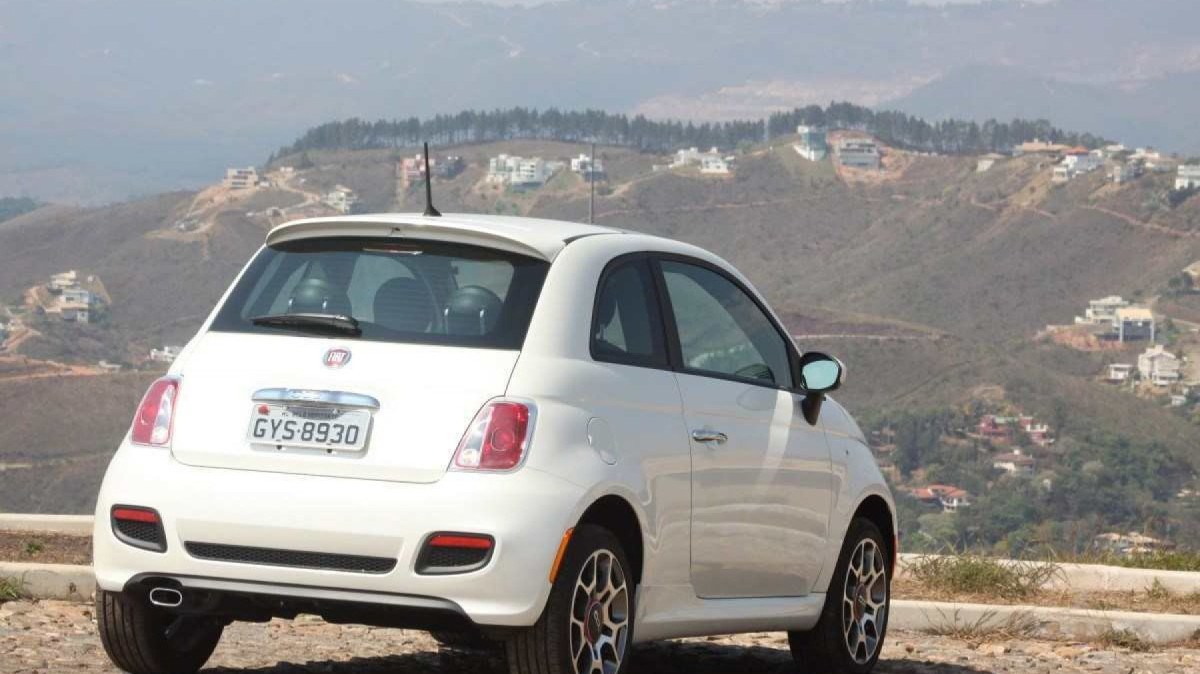 Fiat 500 Sport Air 1.4 16V modelo 2012 branco de traseira estático no calçamento com morro e casas ao fundo