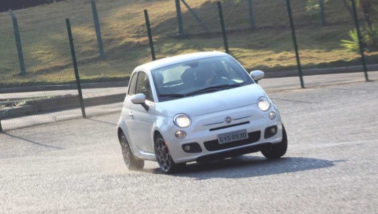 Fiat 500 Sport Air 1.4 16V modelo 2012 branco de frente em movimento no asfalto com gradeado ao fundo