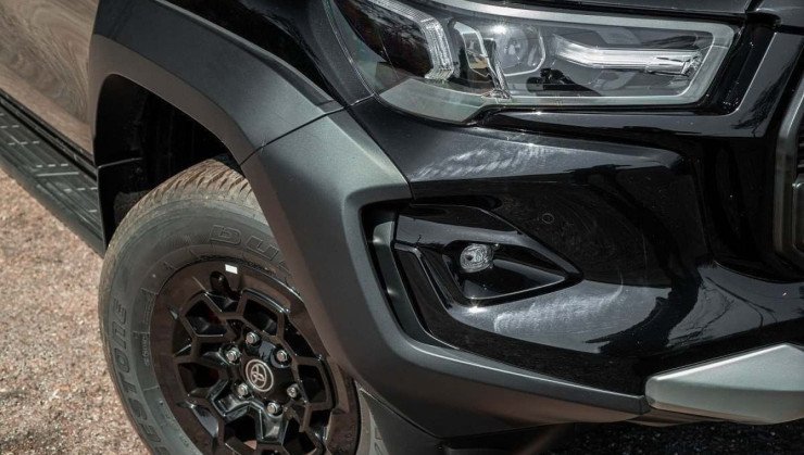 Detalhe da dianteira da Toyota Hilux GR-Sport, mostrando faróis, moldura no para-lama dianteiro e roda de liga leve de 17 polegadas, pintada de preto