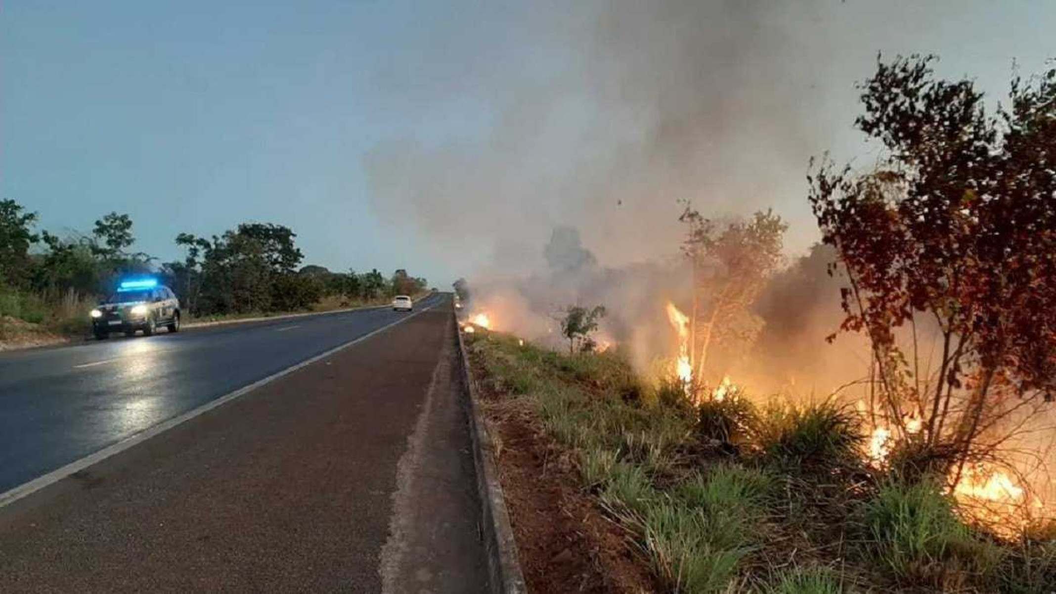 Queimada na beira da estrada com fumaça e carro trafegando no asfalto