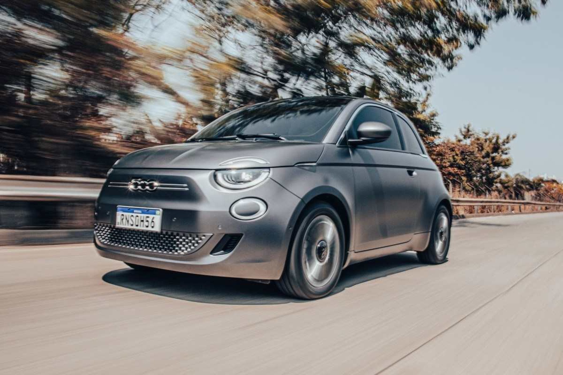 Fiat 500e modelo 2021 hatch elétrico cinza de frente em movimento no asfalto com mato ao fundo