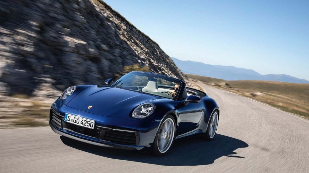 Porsche 911 Cabriolet azul, de frente, movendo-se em uma estrada sinuosa, com a capota abaixada