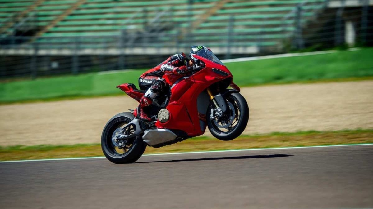 Red Ducati Panigale V4 S 2025 lateralmente em movimento elevando sua frente com a roda dianteira no ar na pista de corrida