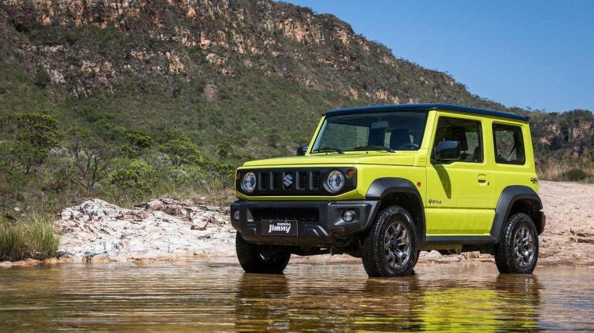 Suzuki Jimny Sierra 4Style amarelo, de frente, estacionado sobre curso d'água, com montanha ao fundo 