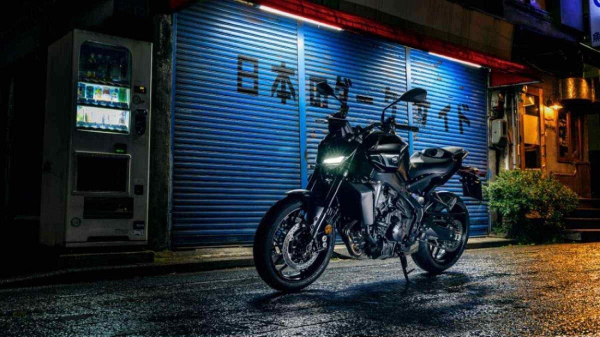 Yamaha MT-09 Y-AMT modelo 2024 preta com frente estática no asfalto com porta de aço azul ao fundo