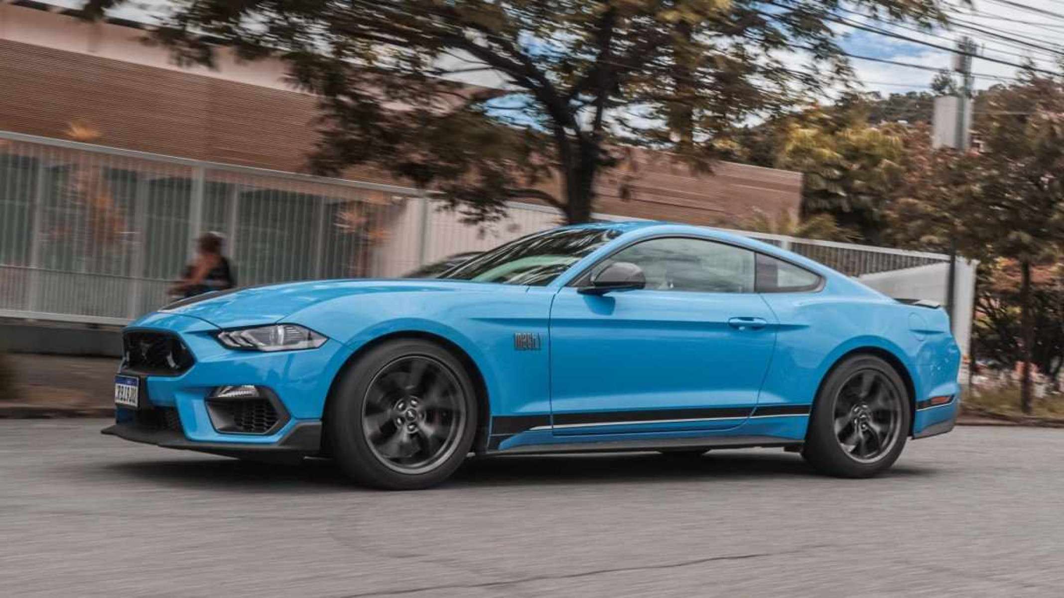 Blue Ford Mustang movendo-se lateralmente na rua de asfalto com casas ao fundo