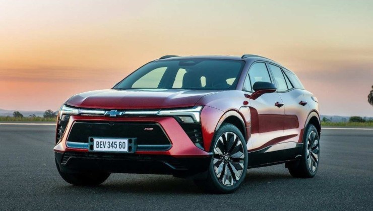 Chevrolet Blazer EV vermelha, de frente, estacionada em local descampado e asfaltado, com pÇor do sol ao fundo