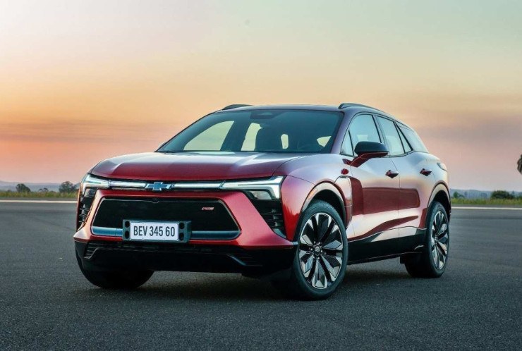 Chevrolet Blazer EV vermelha, de frente, estacionada em local descampado e asfaltado, com pÇor do sol ao fundo