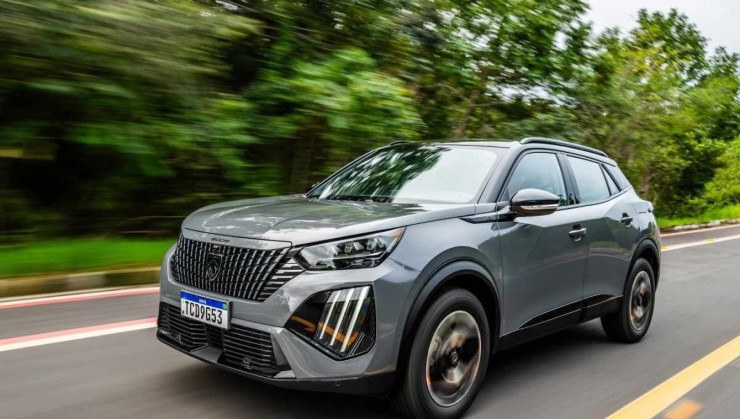 Peugeot 2008 modelo 2025 cinza de frente em movimento no asfalto com mata ao fundo