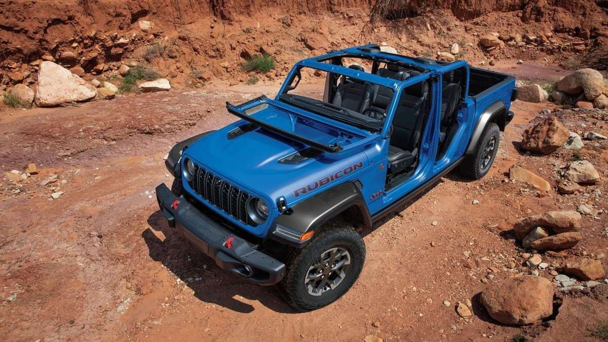 Jeep Gladiator Rubicon 2025 azul visto por cima está estacionado em chão de terra vermelha. 