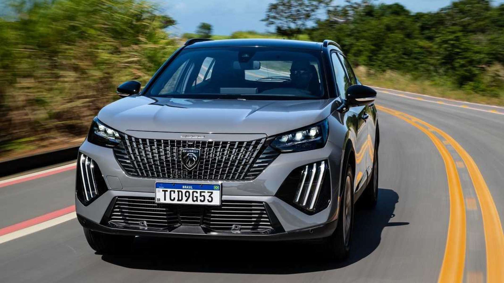 Peugeot 2008 modelo 2025 de frente em movimento no asfalto com mato ao fundo