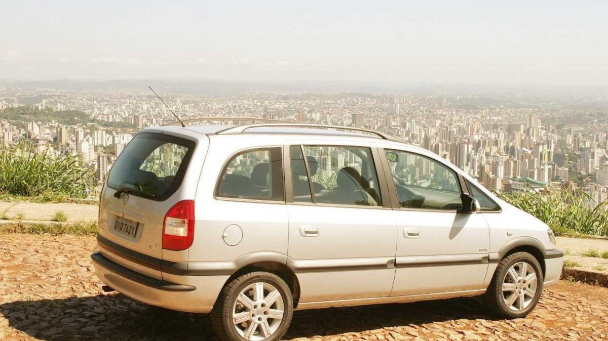 Chevrolet Zafira flex modelo 2004 prata de traseira lateral estática no calçamento com vista da cidade ao fundo
