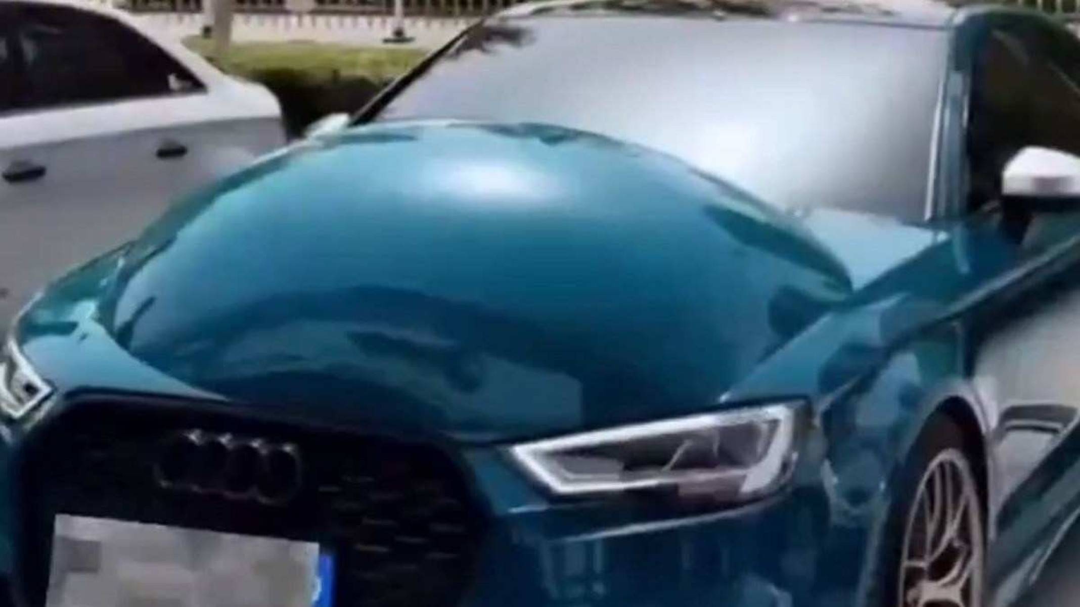 Modelo Audi azul é visto pela dianteira com grande bolha em seu capô. Veículo está estacionado e carro branco e visto ao seu lado esquerdo