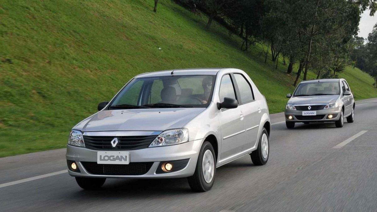 Silver Renault Logan visto viajando em uma estrada pavimentada. O veículo foi fotografado com a frente e a lateral esquerda visíveis. Do lado esquerdo da fotografia há um morro gramado e ao fundo, no canto direito da imagem, outro Logan prateado acompanha o principal.