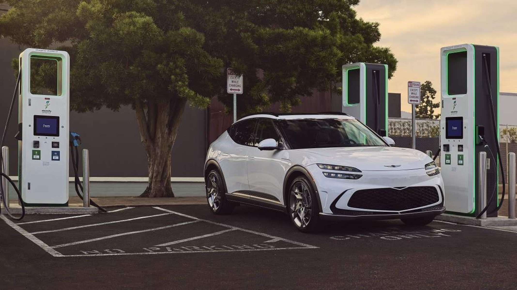 Carro elétrico branco estacionado em uma estação de carregamento com árvores ao fundo