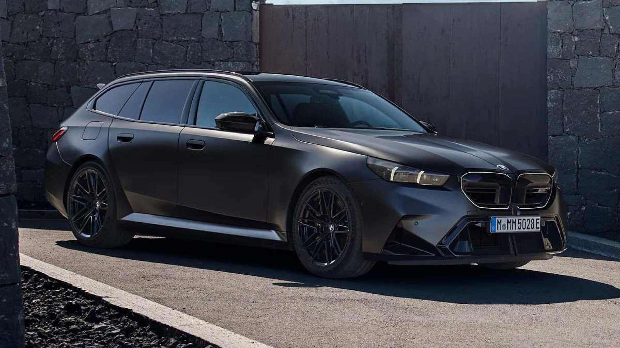 BMW M5 Touring cinza escuro parada em chão de concreto e muro ao fundo