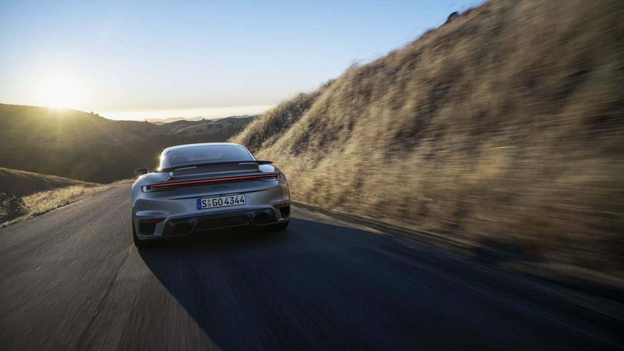 Porsche 911 Turbo 50 Years de traseira em movimento em estrada asfaltada com grama e morro ao lado e ao fundo céu azul