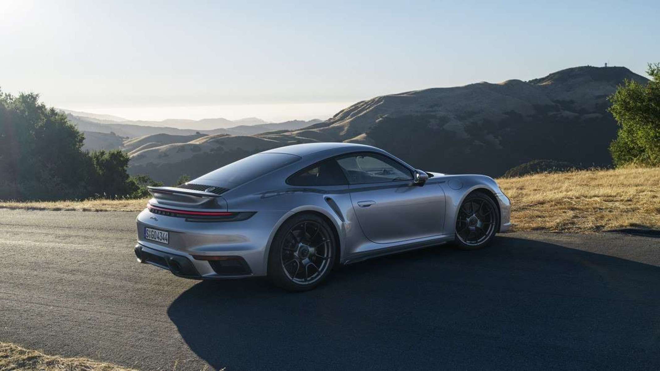 Porsche 911 Turbo 50 Anos parado em estrada asfaltada com grama ao lado, montanhas ao fundo e céu azul