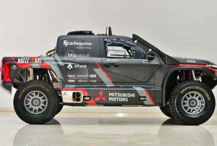 Mitsubishi L200 Triton adesivada em cinza com detalhes em vinho visto pela lateral direita. Picape está estacionada em chão de mármore branco e parede na mesma cor ao fundo