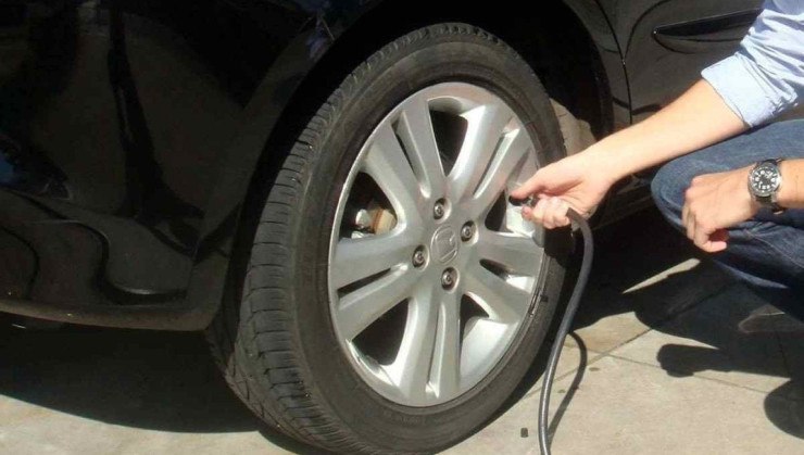 Calibragem de pneus: foto mostra m&atilde;o de um homem segurando mangueira de calibrador acoplada a v&aacute;lvula de pneu de carro preto