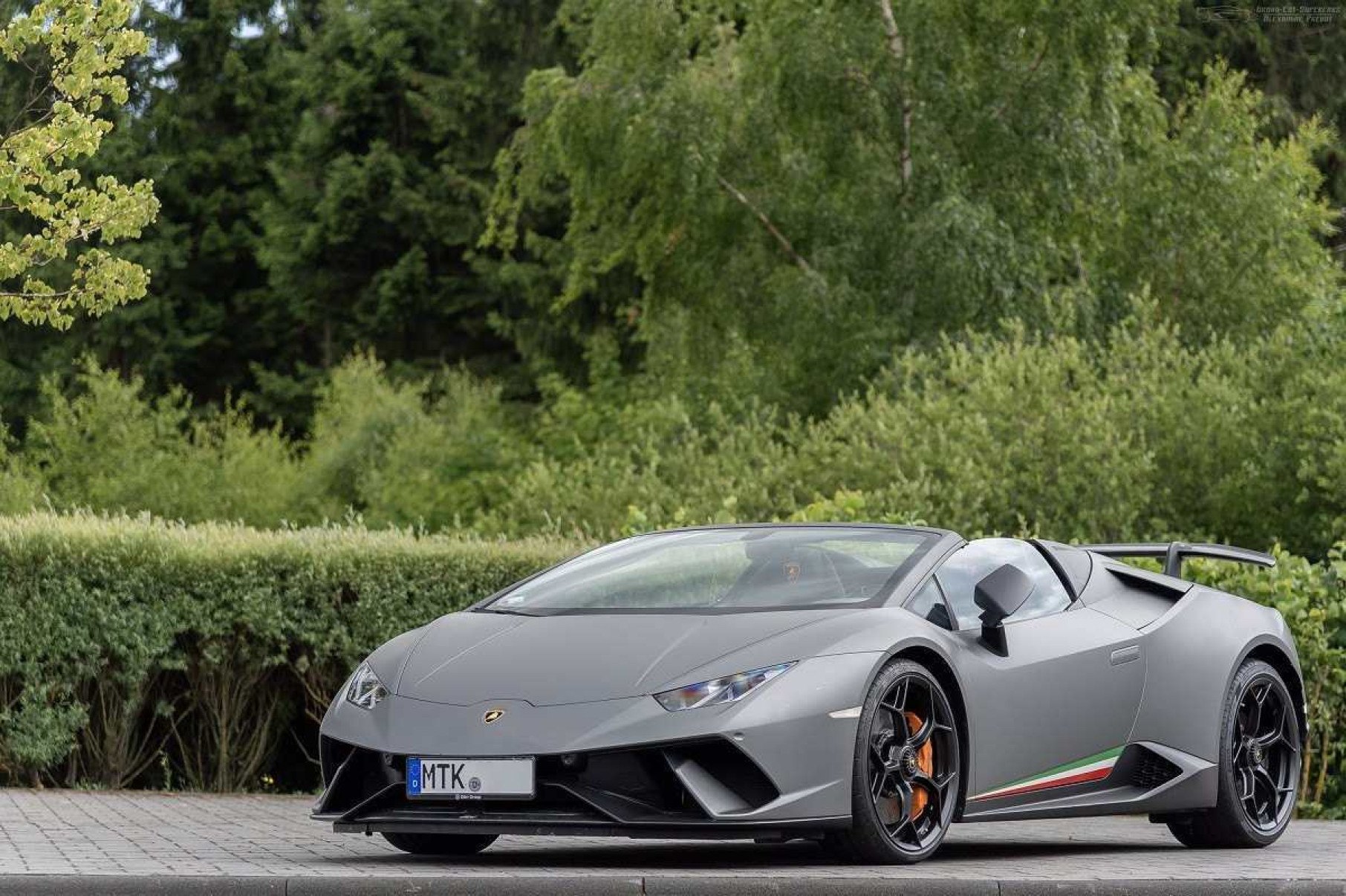 Lamborghini Huracán cinza visto de frente com detalhes da lateral esquerda. Veículo é visto em via asfaltada com árvores ao fundo.