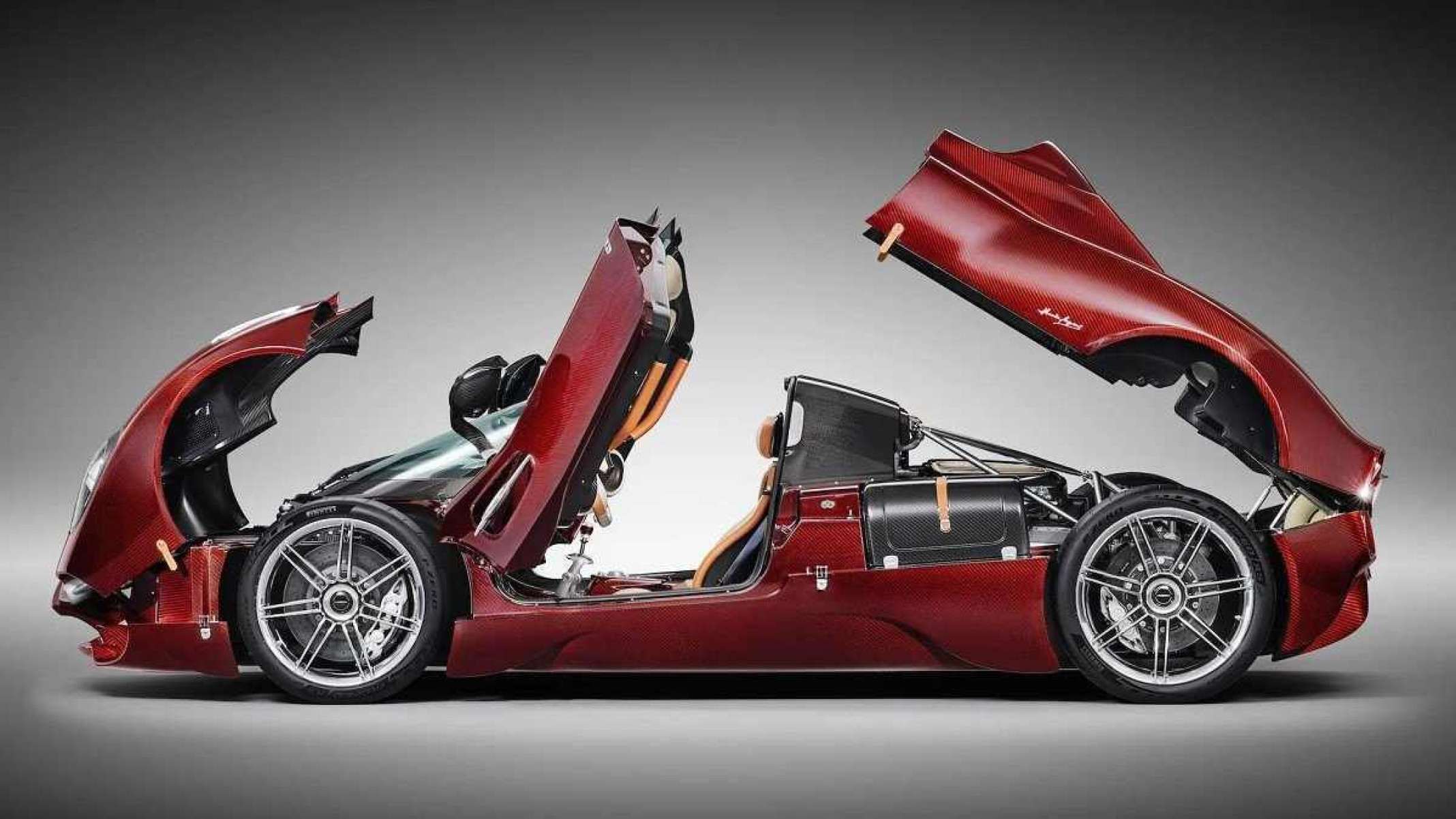 Modelo Pagani vermelho visto de lado com portas, capô e porta-malas abertos. O veículo está estacionado em um fundo branco com sombras ao seu redor. 