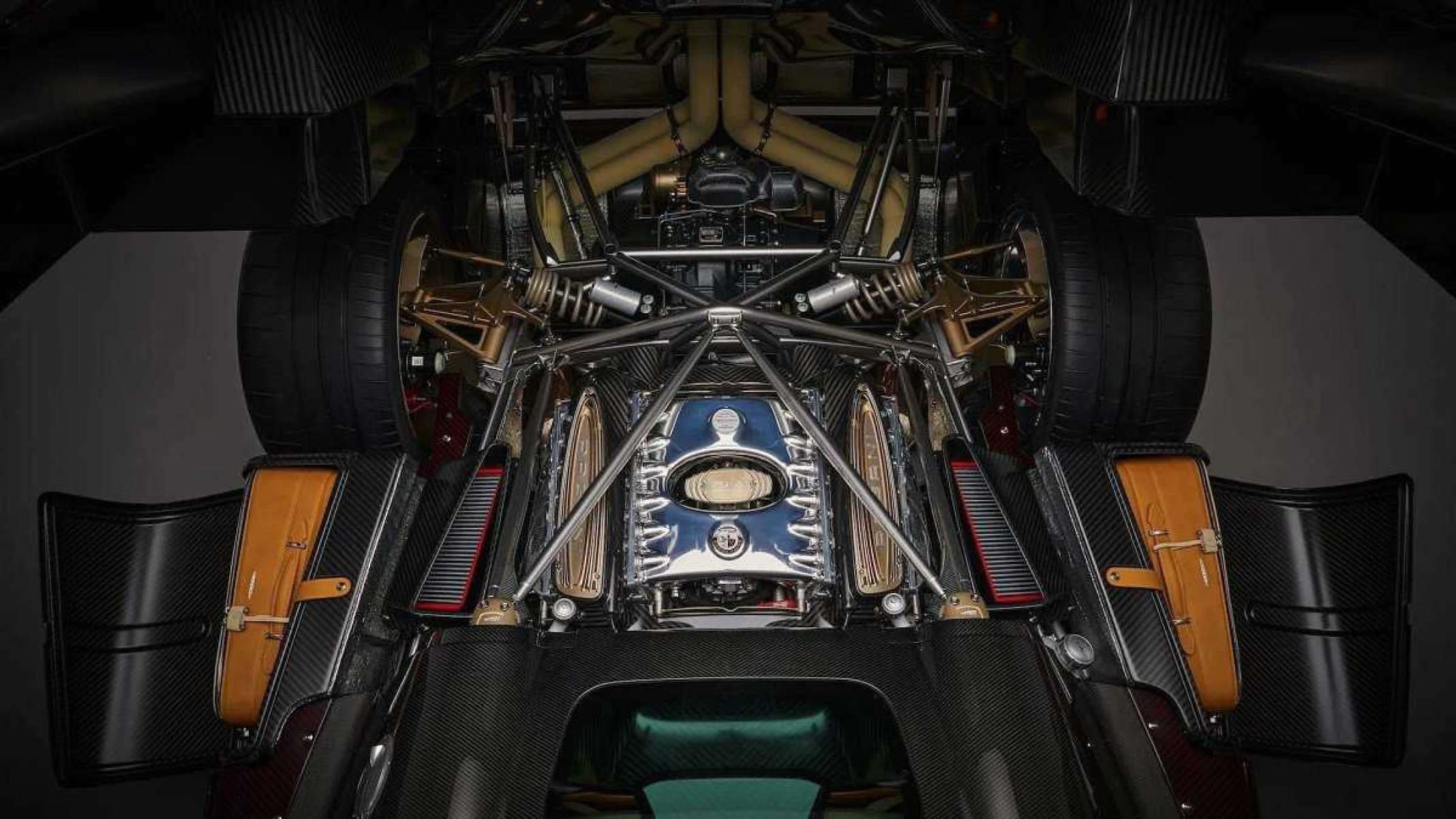 Motor V12 de carro da Pagani. Equipamento é preto com detalhes em prata e laranja. 