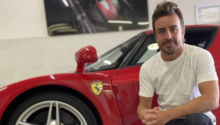 Fernando Alonso, piloto de Fórmula 1 agachado ao lado de uma Ferrari Enzo vermelha, com foco no logotipo da equipe em amarelo