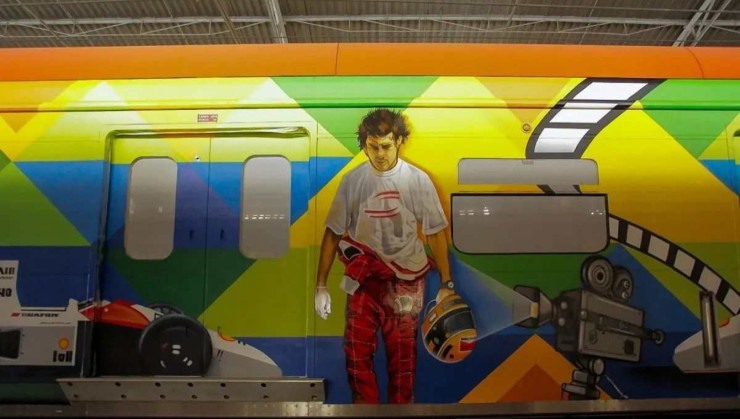 Trem da CPTM em São Paulo com desenho de Ayrton Senna usando camiseta branca e macacão vermelho até a altura da cintura com carro da mclaren ao lado