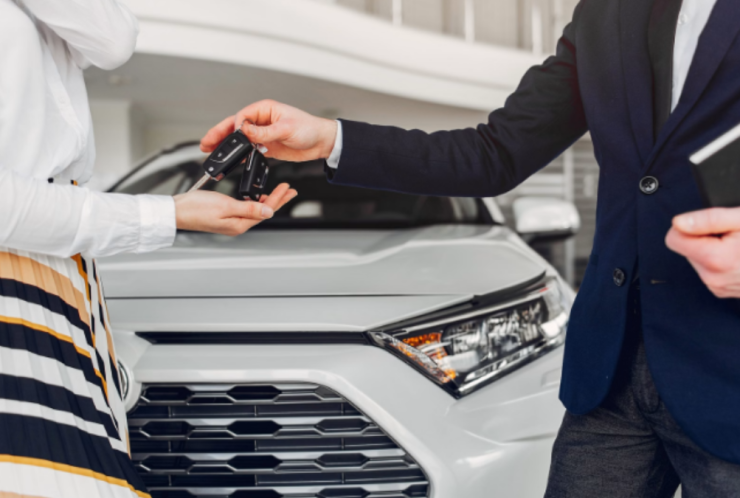 Imagem de um homem e uma mulher entregando chave em frente a carro branco 