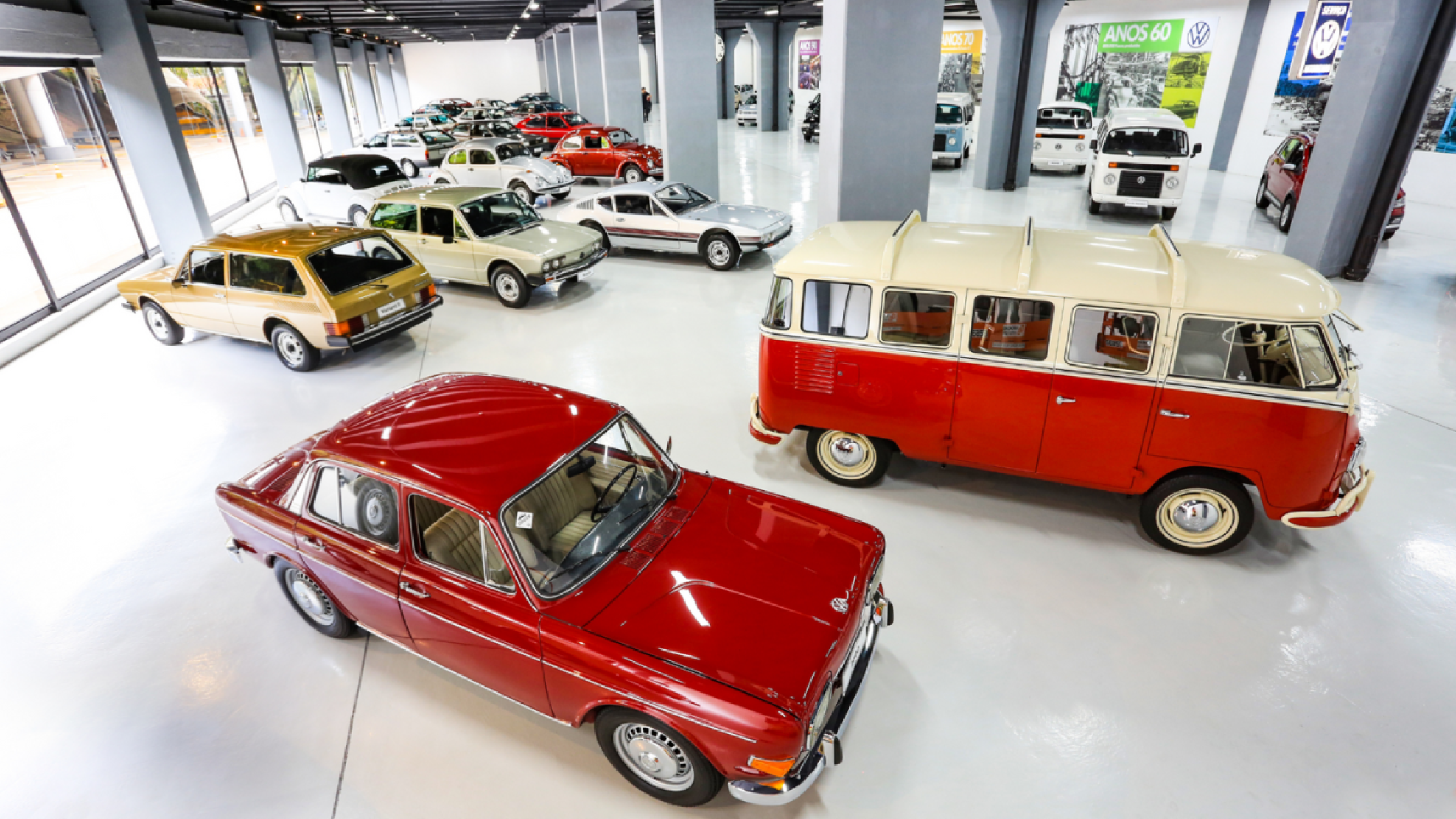 carros volkswagen expostos em galpão. No primeiro plano um TL vermelho ao lado de uma Kombi com teto branco e carroceria vermelha