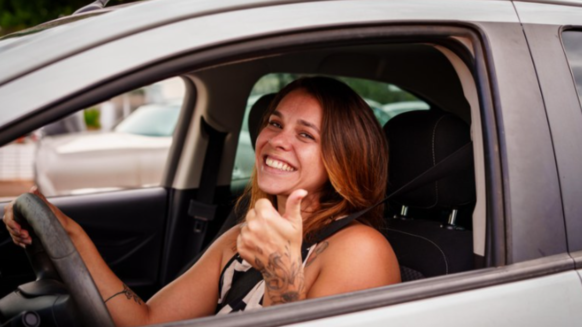 Aluna de autoescola dirige com uma mão no volante